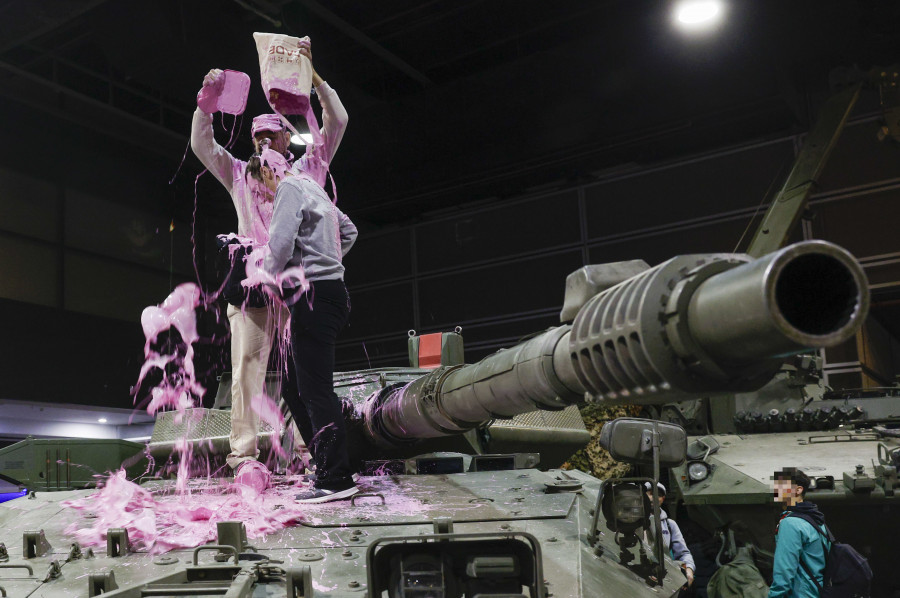 Antimilitaristas vestidos de payaso pintan de rosa un tanque en una feria en València