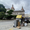 Una mujer camina por delante de un contenedor rebosante de basura detrás del palacio municipal de María Pita