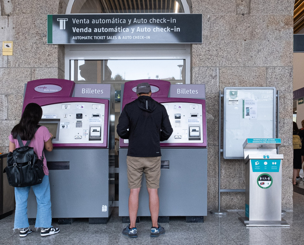 Dos personas compran billetes en los cajeros de venta automática en la estación de trenes, a 24  de agosto de 2022, en Santiago de Compostela, ep