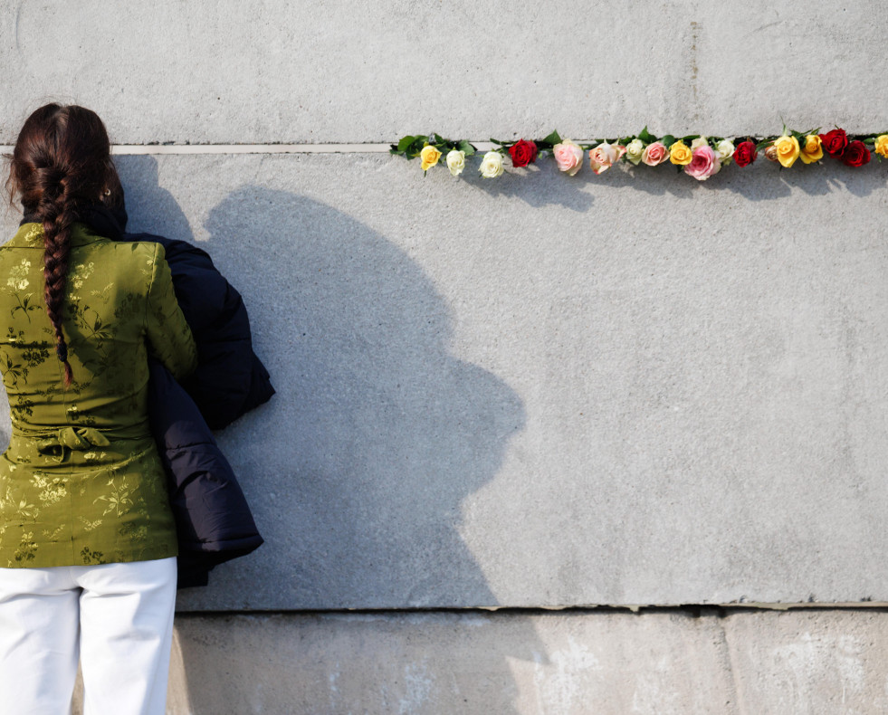 Berlin (Germany), 09/11/2024.- A visitor looks through a gap in remains of the Berlin Wall beside roses after a commemorative event on the 35th anniversary of the fall of the Berlin Wall in Berlin, Ge