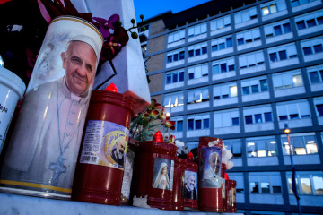 Rome (Italy), 22/02/2025.- A candle with the image of Pope Francis (L) sits at the foot of the statue of Pope St. John Paul II outside Gemelli University Hospital, where Pope Francis is battling pneum